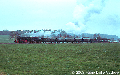 Zum Vergr&ouml;&szlig;ern klicken - Bei leichtem Schneetreiben kommt die 52 7596 mit ihren 7 Wagen aus Bad Wurzach (Mennisweiler, 06. April 2003).